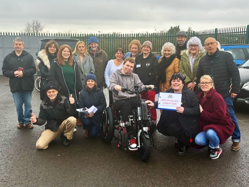 Connor Head picks up his new electric wheelchair from volunteers at the Barton Hill RFC Charity Cafe